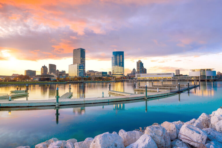 Milwaukee skyline at twilight with city reflection in lake Michigan and harbor pier.