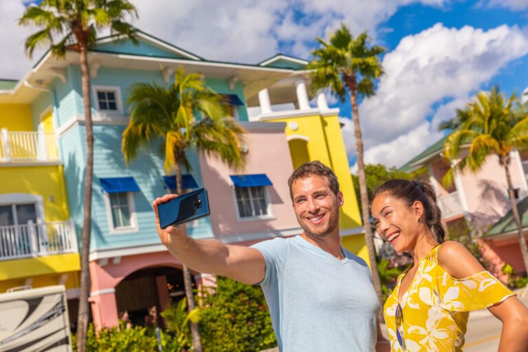 Selfie photo couple tourists taking picture with smart phone in Fort Myers, Florida at colorful wood beach cottages. USA summer travel lifestyle.